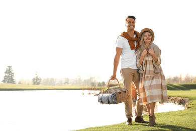 Photo of Young couple with picnic basket near lake on sunny day