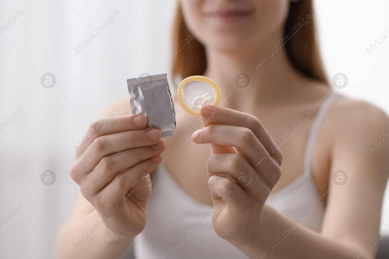 Photo of Woman holding unwrapped condom indoors, closeup. Safe sex