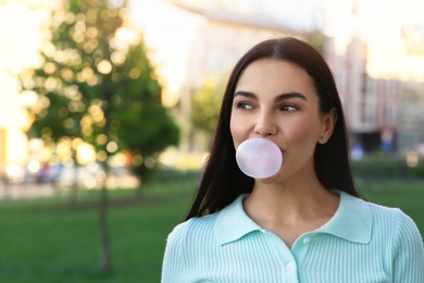 Photo of Beautiful woman blowing gum in park, space for text