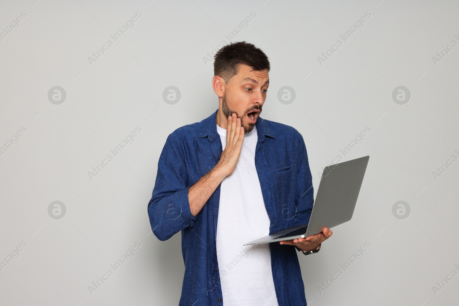 Photo of Emotional man with laptop on light grey background