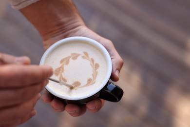 Photo of Barista creating pattern in cup of coffee on blurred background, closeup. Space for text