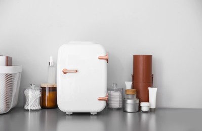 Photo of Cosmetics refrigerator and skin care products on grey vanity table indoors