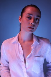 Portrait of beautiful young woman on blue background with neon lights