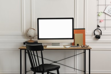 Photo of Stylish workspace with computer and stationery on wooden desk near white wall indoors
