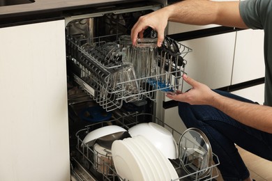 Photo of Man loading dishwasher with glasses in kitchen, closeup