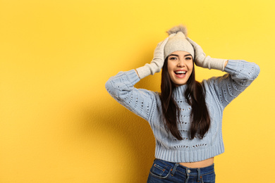 Photo of Happy young woman in warm clothes on yellow background, space for text. Winter vacation