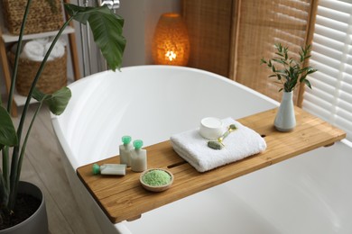 Wooden tray with spa products and green branches on bath tub in bathroom
