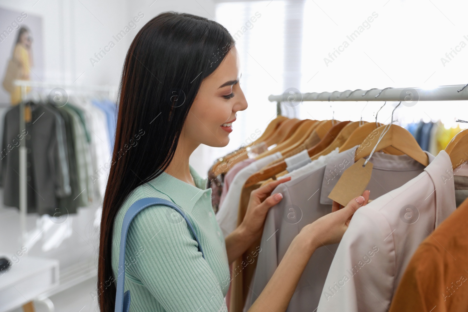 Photo of Young woman choosing clothes near rack in modern boutique