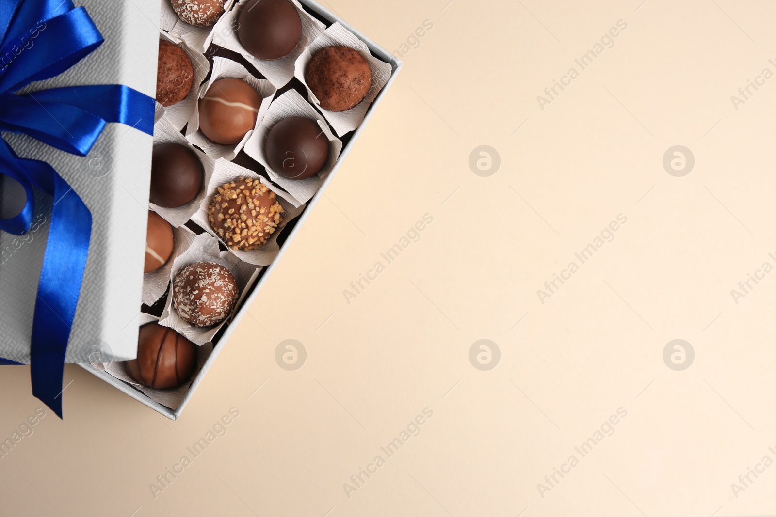 Photo of Box with delicious chocolate candies on beige background, top view. Space for text