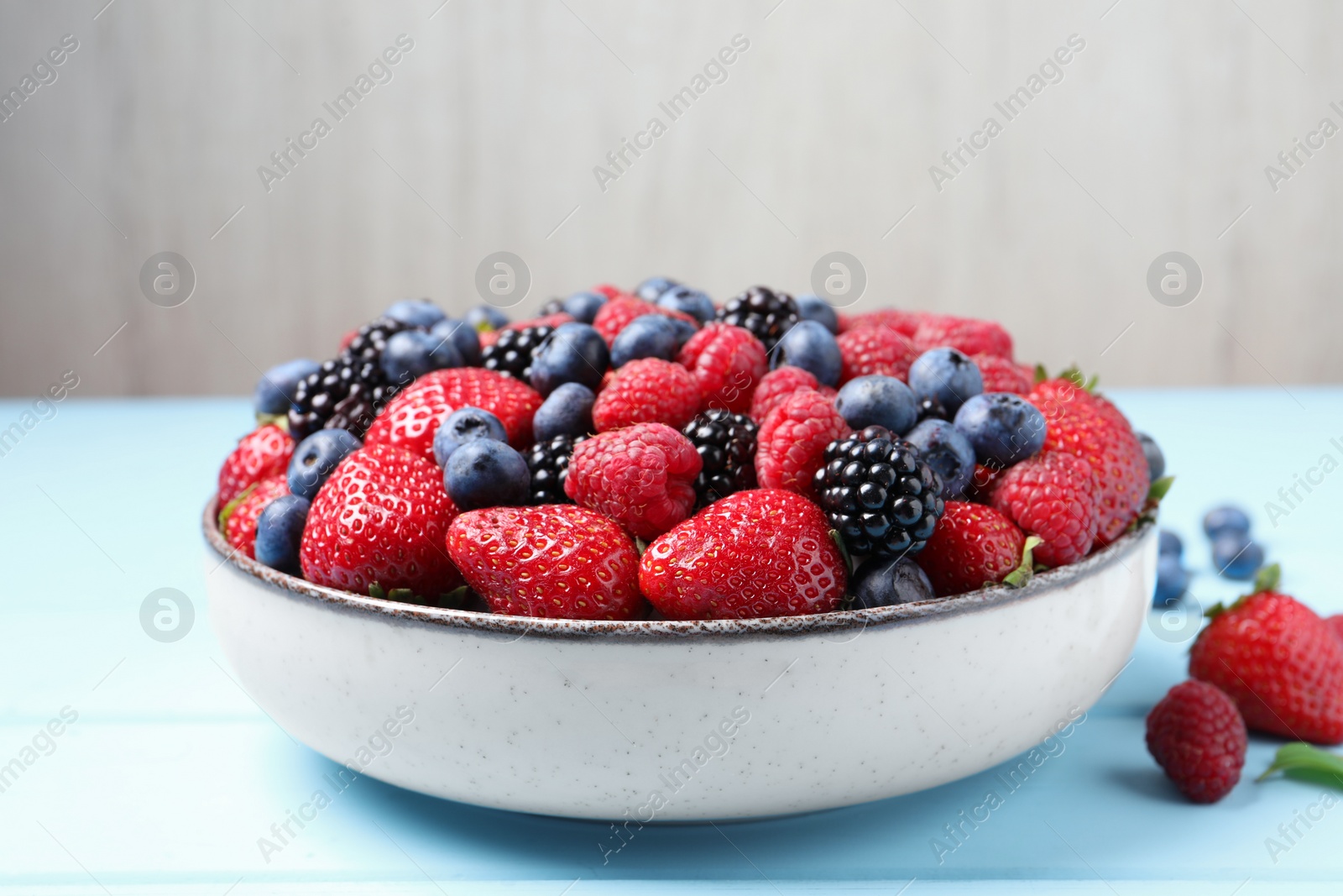 Photo of Different fresh ripe berries on light blue wooden table, closeup