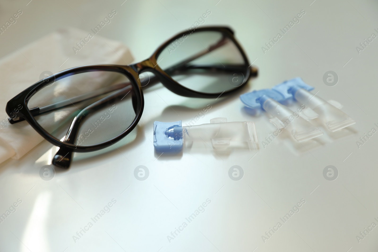 Photo of Single dose eye drops, glasses and fabric on white table, closeup