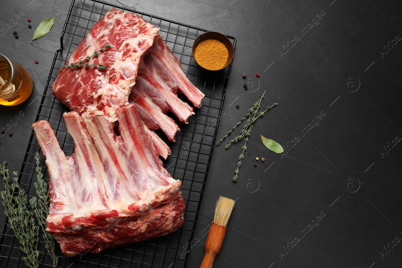 Photo of Raw ribs with thyme and pepper on black table, flat lay