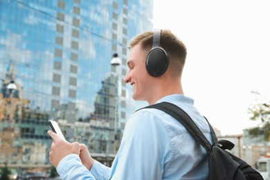 Smiling man in headphones using smartphone on city street. Space for text