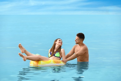 Happy woman in bikini floating on inflatable ring and her boyfriend in sea. Lovely couple