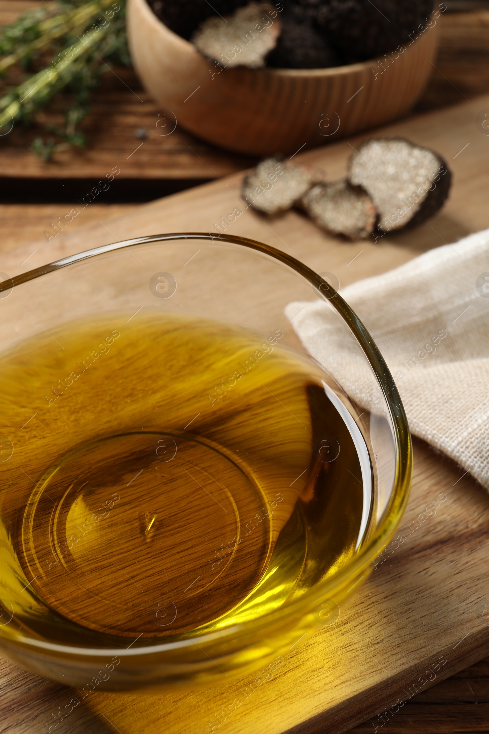 Photo of Fresh truffle oil in glass bowl on wooden board, closeup