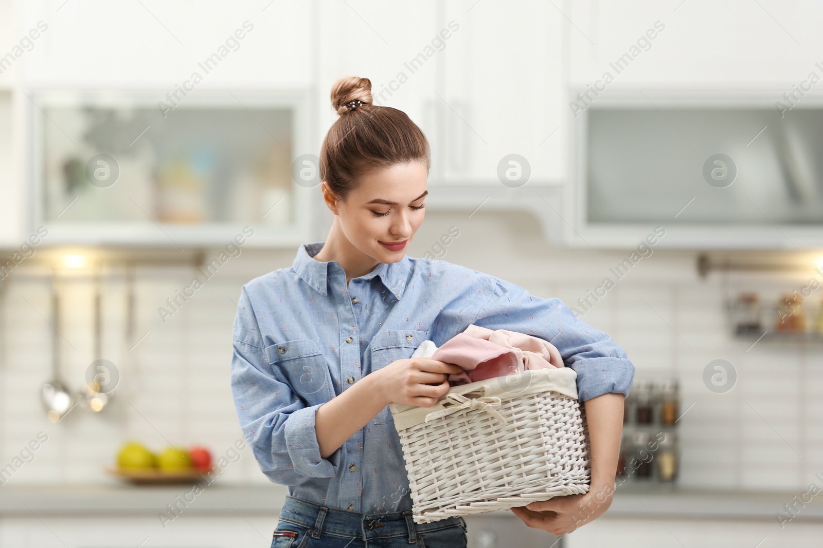 Woman holding wicker basket with dirty laundry in kitchen Photo of Woman holding wicker basket with dirty laundry in kitchen