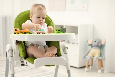 Children toys. Cute little boy playing with toy cars in high chair at home