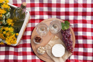 Glasses of white wine and snacks for picnic served on blanket, flat lay
