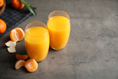 Fresh tangerines and glasses of juice on grey table. Space for text