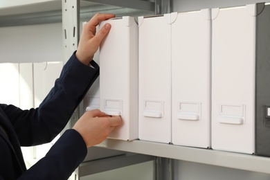 Photo of Woman taking folder with documents from shelf in archive, closeup