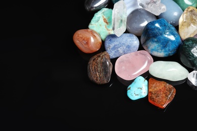 Photo of Different beautiful gemstones on black background. Space for text