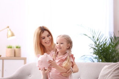 Photo of Mother and daughter with piggy bank at home