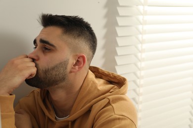 Photo of Sad young man in hoodie at home. Space for text