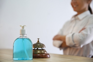Photo of Receptionist at countertop in hotel, focus on dispenser bottle with antiseptic gel and service bell