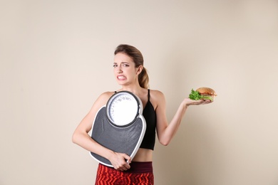 Photo of Young beautiful woman with scales and sandwich on light background. Weight loss motivation