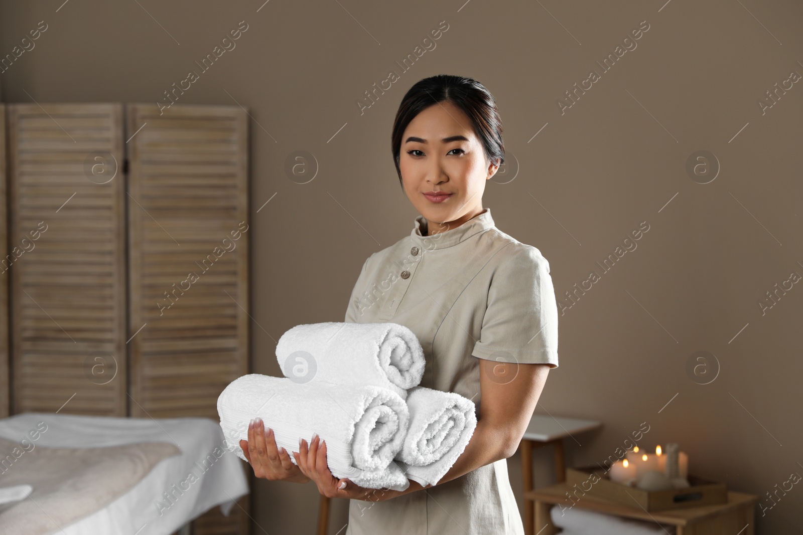 Photo of Portrait of young Asian masseur with towels in spa salon