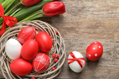 Photo of Flat lay composition of nest with painted Easter eggs and flowers on wooden table, space for text