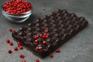 Photo of Delicious chocolate bar and red peppercorns on grey textured table, closeup