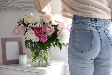 Photo of Woman putting fresh peonies in vase at home, closeup