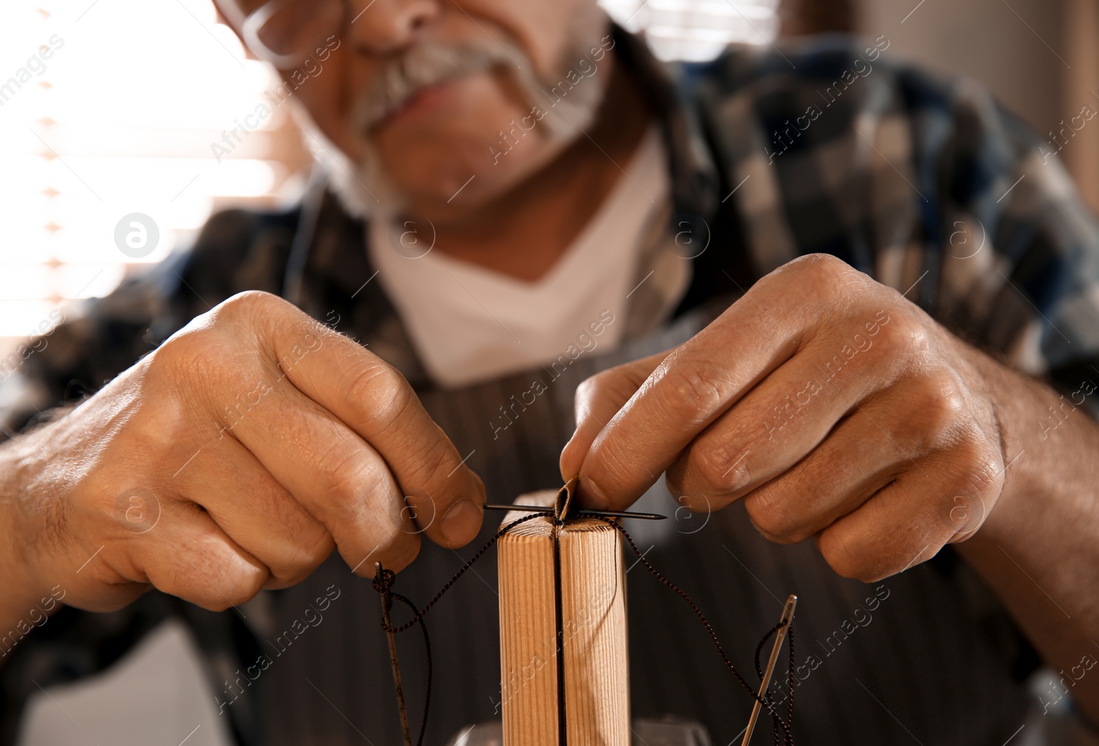 Photo of Man sewing piece of leather in workshop, closeup