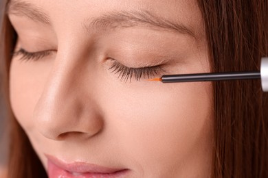 Photo of Woman applying serum onto eyelashes, closeup view