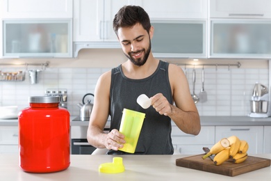 Photo of Young man preparing protein shake at table in kitchen
