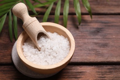 Photo of Sea salt in bowl and green leaves on wooden table, space for text. Spa product