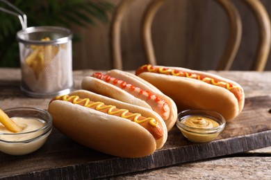 Delicious hot dogs with sauces and French fry on wooden table, closeup