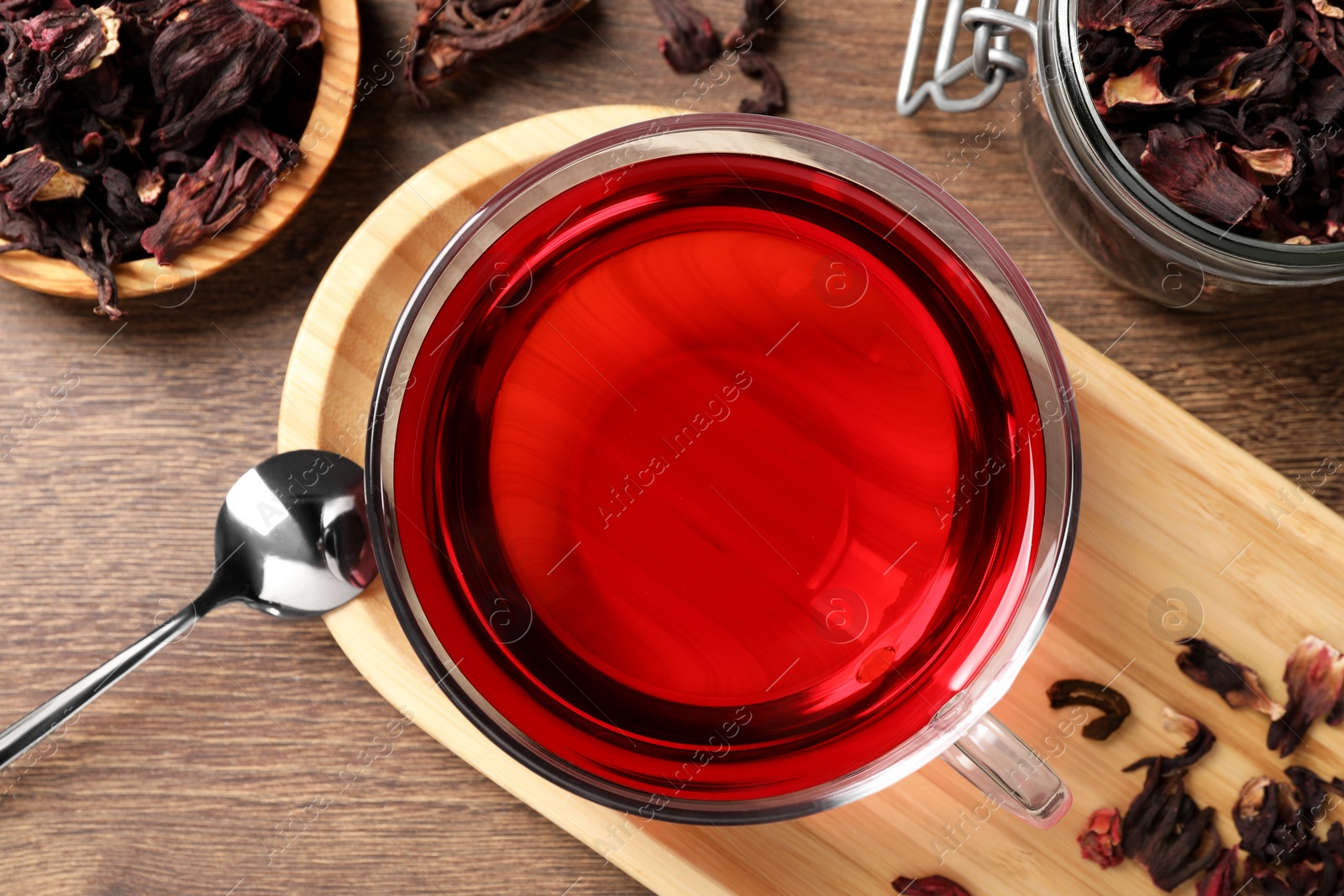 Cup of fresh hibiscus tea, dry flower leaves and spoon on wooden table, flat lay Photo of Cup of fresh hibiscus tea, dry flower leaves and spoon on wooden table, flat lay