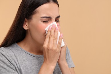 Photo of Suffering from allergy. Young woman blowing her nose in tissue on beige background, closeup. Space for text