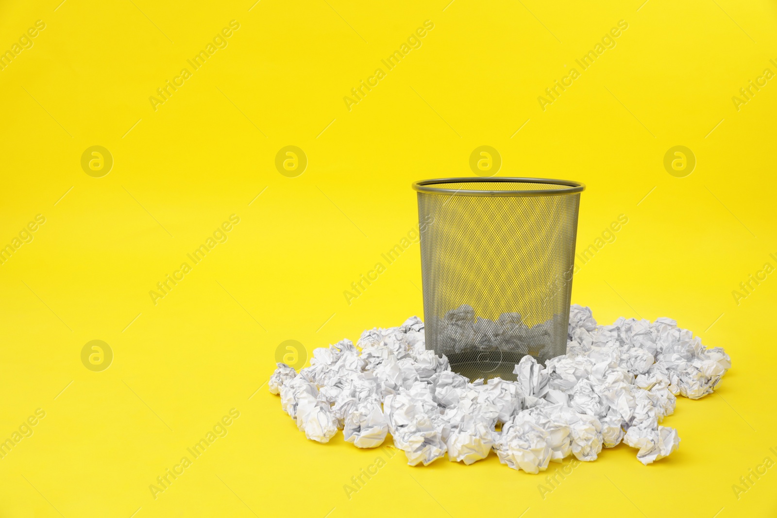 Photo of Metal bin and crumpled paper on color background, space for text