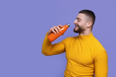 Photo of Handsome man with thermo bottle on purple background, space for text