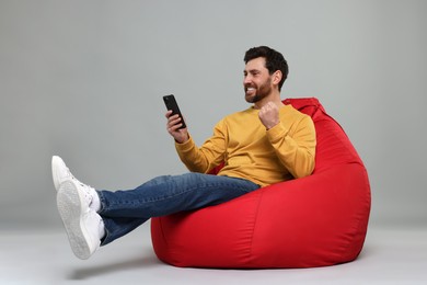 Photo of Happy man with smartphone sitting on bean bag against grey background