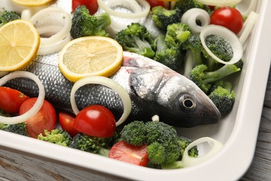 Photo of Raw fish with vegetables and lemon in baking dish on table