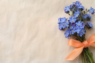 Photo of Beautiful blue forget-me-not flowers tied with ribbon on light background, top view. Space for text