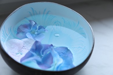 Photo of Spa composition. Aromatic water in bowl and flowers on white table, closeup
