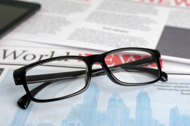 Photo of Stylish glasses on newspaper pages, closeup view