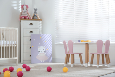 Photo of Crib, table and chairs with bunny ears in stylish baby room interior