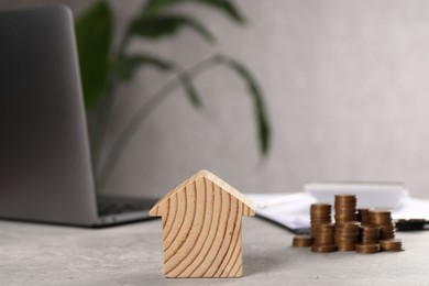 Photo of House model, stacked coins, laptop and clipboard on grey table, selective focus
