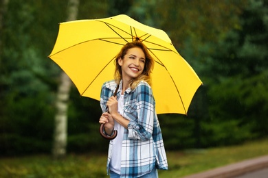 Photo of Happy young woman with umbrella under rain in park